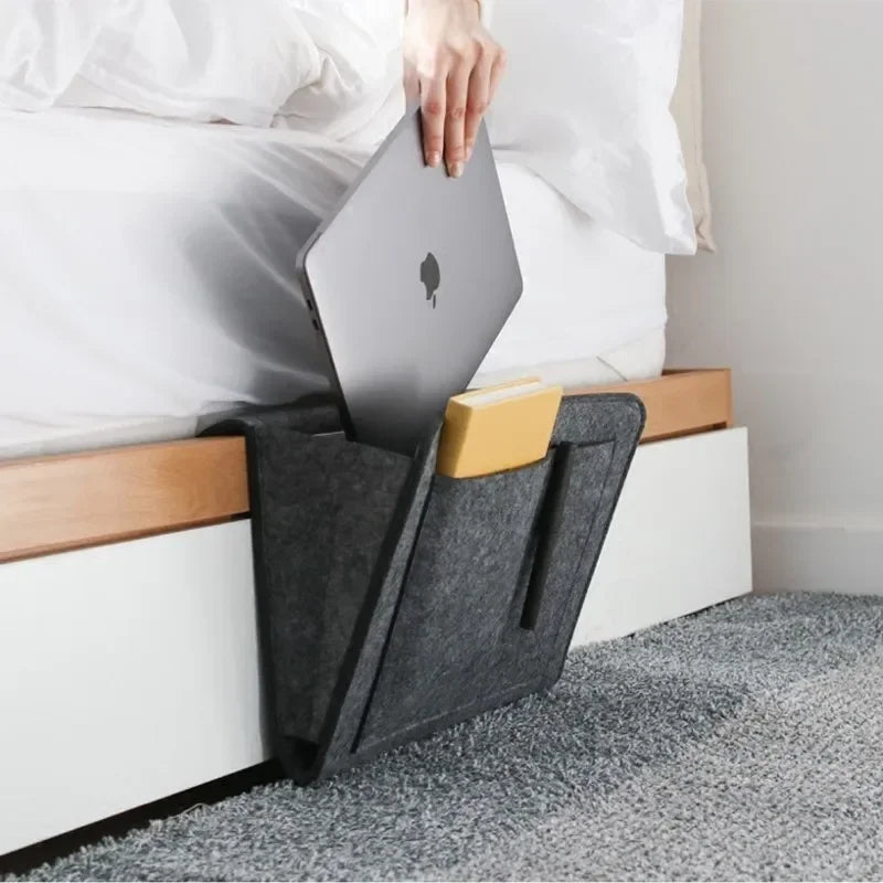 Plyzo bedside organizer caddy hanging on a bed frame holding phone, remote, and book